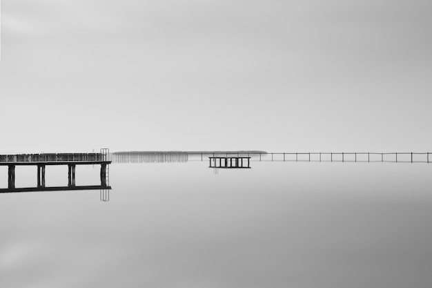 Free Photo greyscale shot of a wooden pier near the sea under the beautiful cloudy sky