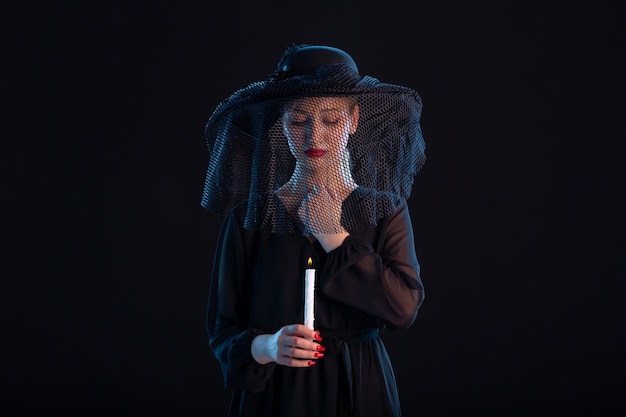 Free photo grieving female dressed in black with burning candle on a black  sadness funeral death