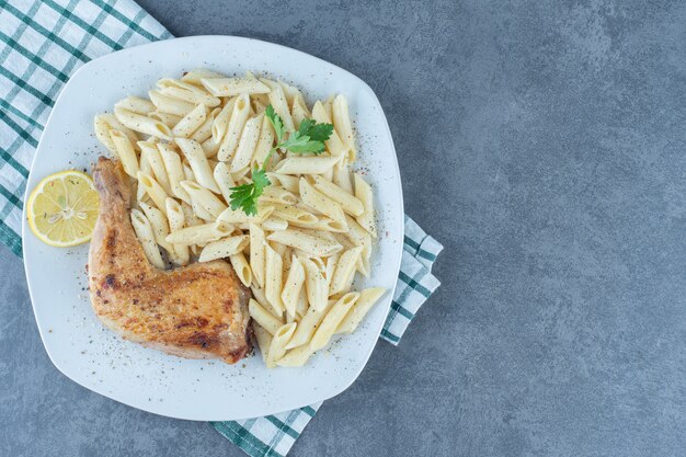 Grilled chicken leg and penne pasta on white plate. 