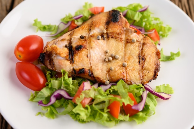 Grilled chicken on a white plate with a salad of tomatoes, carrots and chilies cut into pieces.