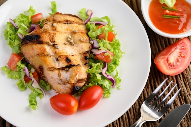 Grilled chicken on a white plate with a salad of tomatoes, carrots and chilies cut into pieces.