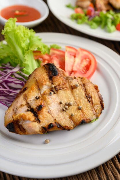 Grilled chicken on a white plate with a salad of tomatoes, carrots and chilies cut into pieces.