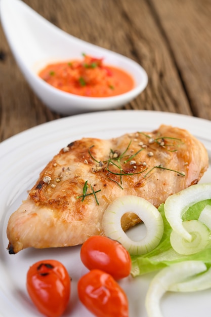 Free Photo grilled chicken on a white plate with tomatoes, salad, onion and chili sauce.