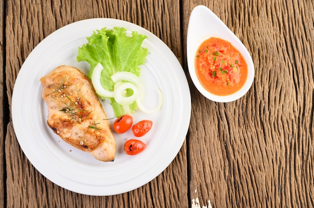 Grilled chicken on a white plate with tomatoes, salad, onion and chili sauce.