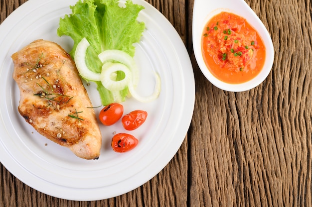 Grilled chicken on a white plate with tomatoes, salad, onion and chili sauce.