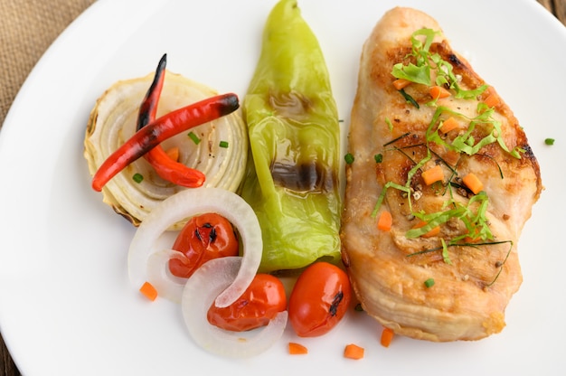 Grilled chicken on a white plate with tomatoes, salad, onion, chili and sauce.