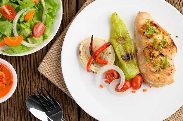 Grilled chicken on a white plate with tomatoes, salad, onion, chili and sauce.