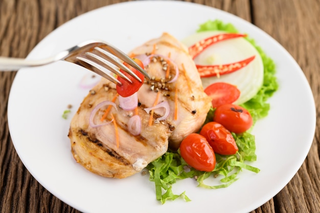 Grilled chicken on a white plate with tomatoes, salad, onion, chili and sauce.