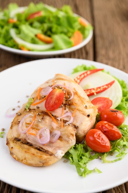 Grilled chicken on a white plate with tomatoes, salad, onion, chili and sauce.