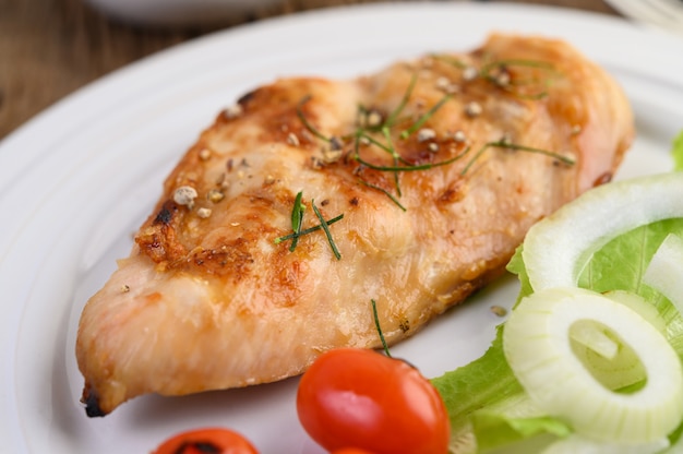 Grilled chicken on a white plate with tomatoes, salad and onion.