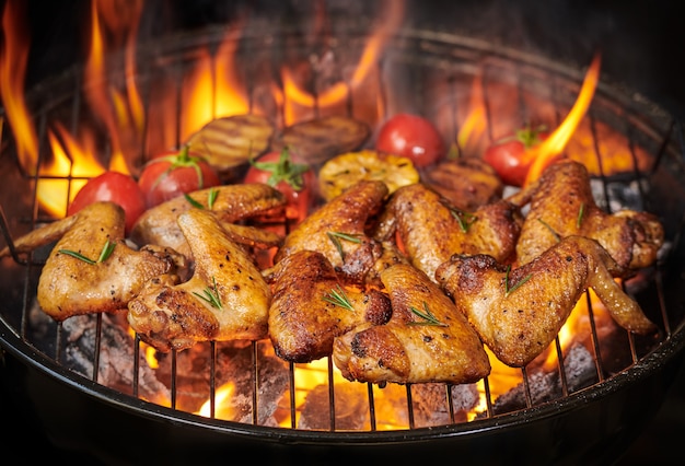 Free photo grilled chicken wings on the flaming grill with grilled vegetables in barbecue sauce with pepper seeds rosemary, salt. top view with copy space.