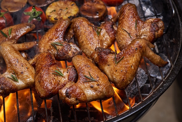 Free photo grilled chicken wings on the flaming grill with grilled vegetables in barbecue sauce with pepper seeds rosemary, salt.