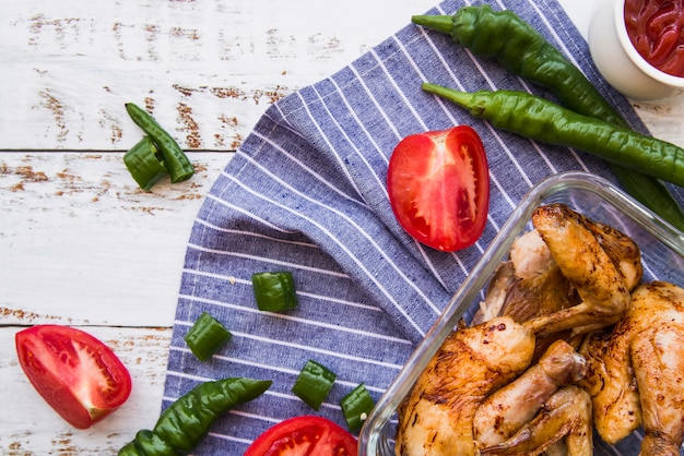 Free Photo grilled chicken wings and slices of tomatoes; green chilies on wooden table