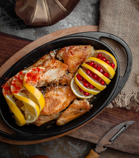 Grilled chicken with lemon and pomegranate seeds inside black iron pan.