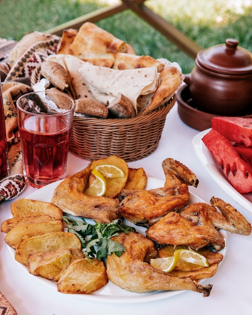 Free photo grilled chicken with potato slices served with lemon,herbs, glass of red drink and bread.