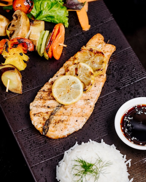 Free photo grilled fish fillet with lemon, vegetable stick grill, rice and sauce.