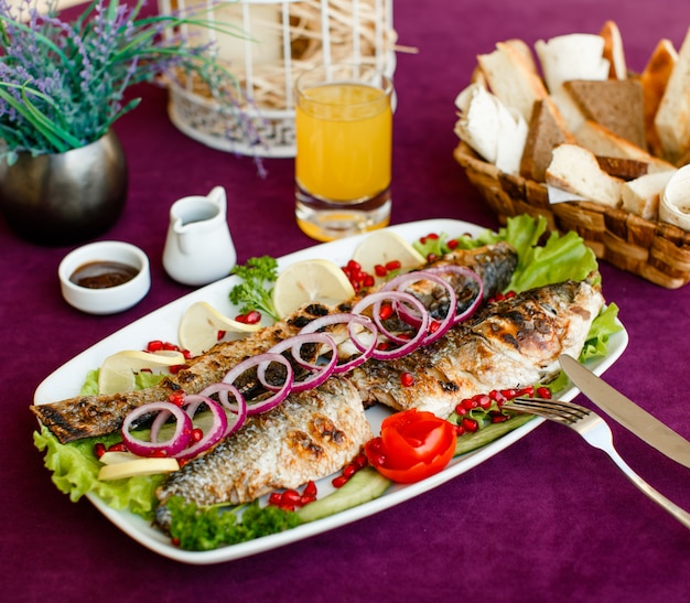 Grilled fish garnished with red onion, tomato, lettuce, lemon and pomegranate