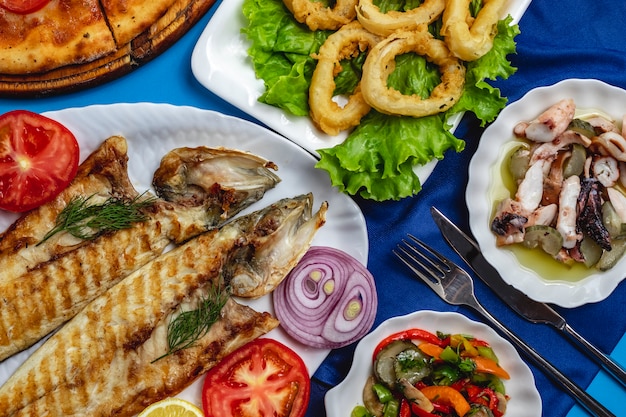 Grilled fish tomato onion calamary green salad top view