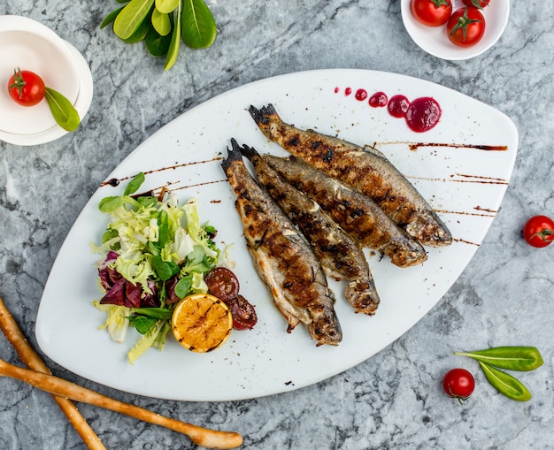 Free photo grilled fish with vegetable salad and orange.