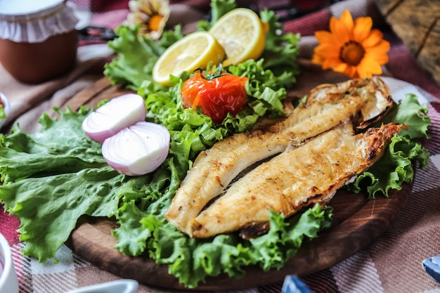 Free photo grilled fish on the wooden board onion lettuce tomato lemon