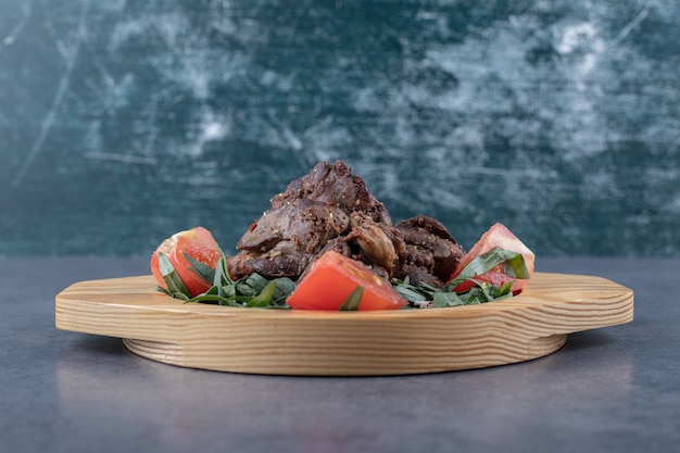 Free photo grilled kebab and tomato slices on wooden plate.