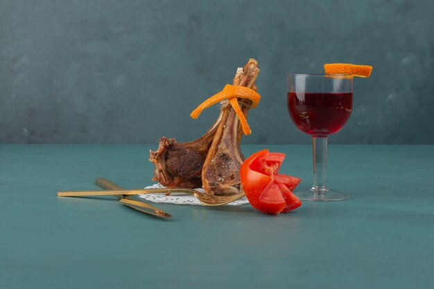 Grilled lamb chops and a glass of juice on blue table.