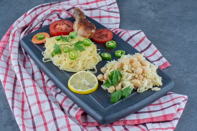 Grilled leg, spaghetti and rice on dark board.