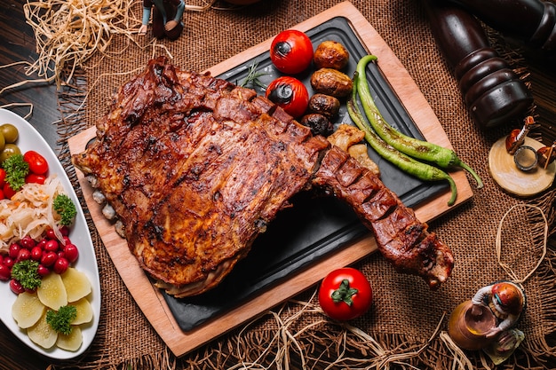 Grilled ribs on the wooden board tomato pepper potato top view