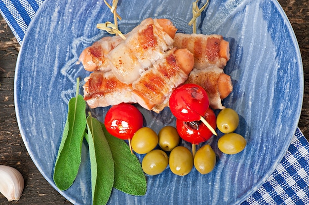 Free Photo grilled sausages wrapped in strips of bacon with tomatoes and sage leaves