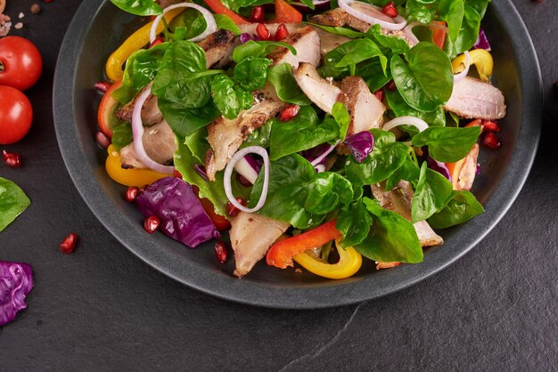 Grilled steak with fresh vegetable, sweet pepper, tomatoes, red onion, pink pepper and spices. Home made tasty food. Concept for tasty and healthy meal. Black stone surface. Pork steak with salad