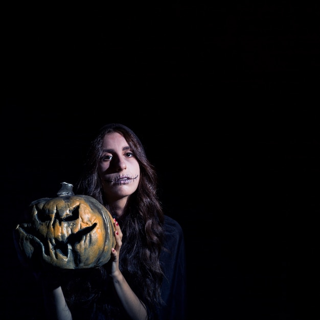 Free photo grim female with scarecrow makeup holding pumpkin