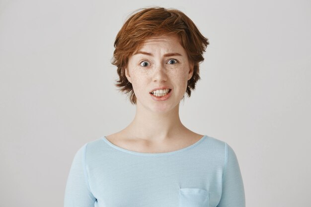 Grimacing redhead girl posing against the white wall