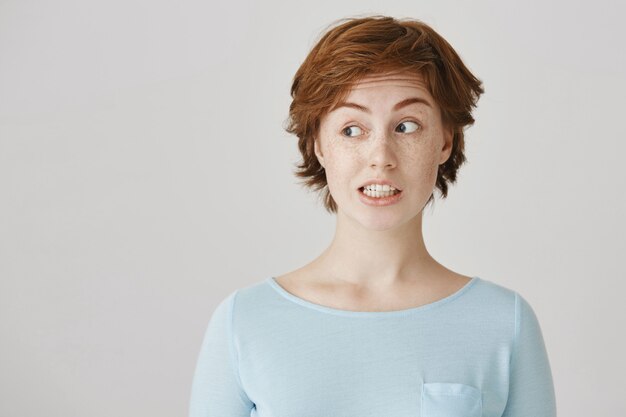 Grimacing redhead girl posing against the white wall