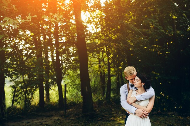 Groom embracing his wife from behind at sunset