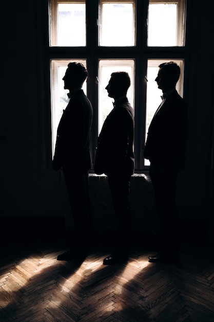 Free photo groom and his two friends stand near a hotel window