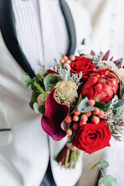 The groom holds a wedding bouquet in his hands