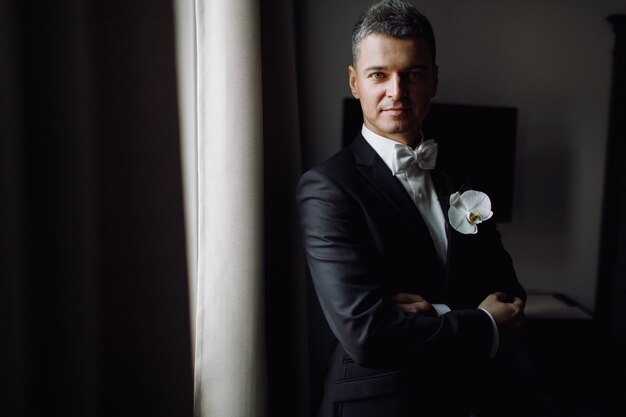 Groom's morning. Handsome man in black tuxedo with white orchid