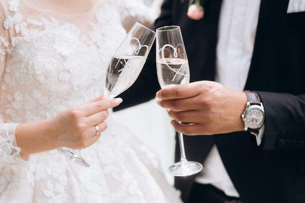 Groom with bride are knocking glasses with champagne