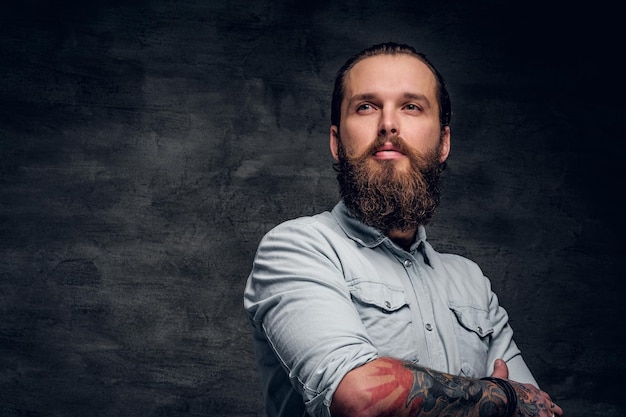 Free photo groomed bearded man with tattooes is posing at dark photo studio.