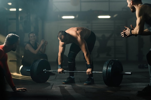 Free photo group of athletes supporting muscular build man who is performing deadlift with barbell in a gym