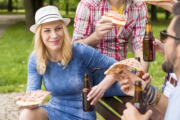 Free photo group of caucasian friends sitting on the bench and enjoying their beer in the park