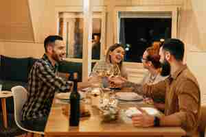 Free photo group of cheerful friends having fun while having dinner and toasting with wine at dining table