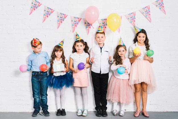 Group of children standing against wall holding balloons in hand at birthday party