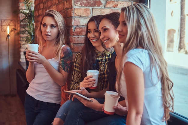 Free photo group of female friends in casual clothes discussing while looking something on a digital tablet in a room with a loft interior.