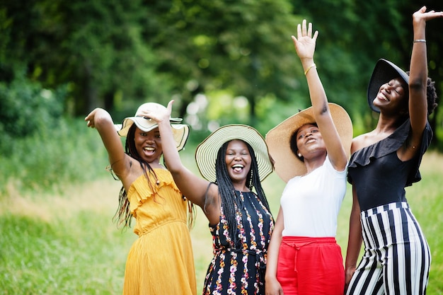 Group of four gorgeous african american womans wear summer hat spending time at green grass in park