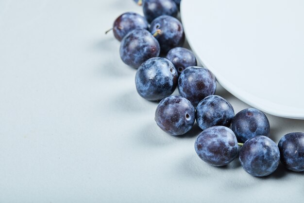 Group of fresh plums around the white plate.