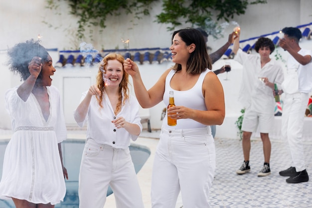 Free photo group of friends having fun during a white party with drinks by the pool