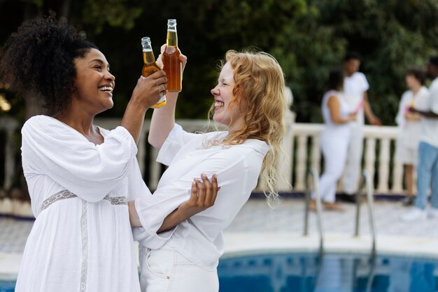 Group of friends having fun during a white party with drinks by the pool