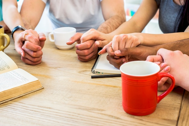 Group of friends holding hands over table with books and cups of beverage