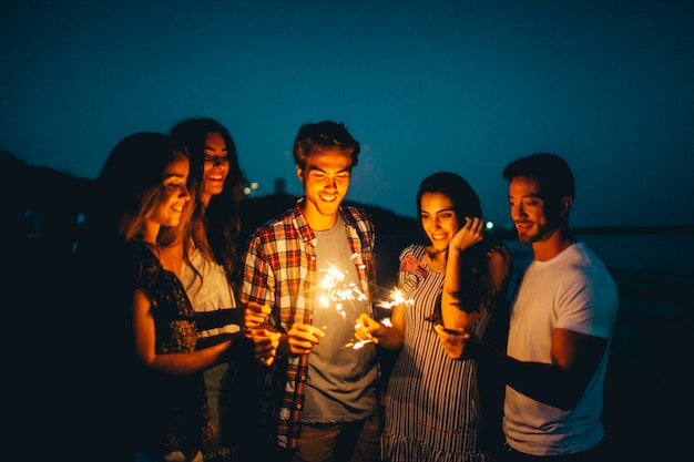 Free photo group of friends with sparkler at a night beach